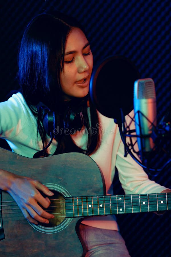 A cute Asian singer and musician playing guitar and sing a song for recording in voice studio