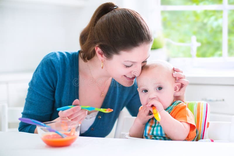 Cute baby boy eating his first solid food with his mother