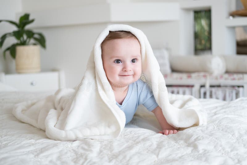 Cute baby boy 6 months old in blu bodysuit smiling and lying on bed with white plaid at home stock photo