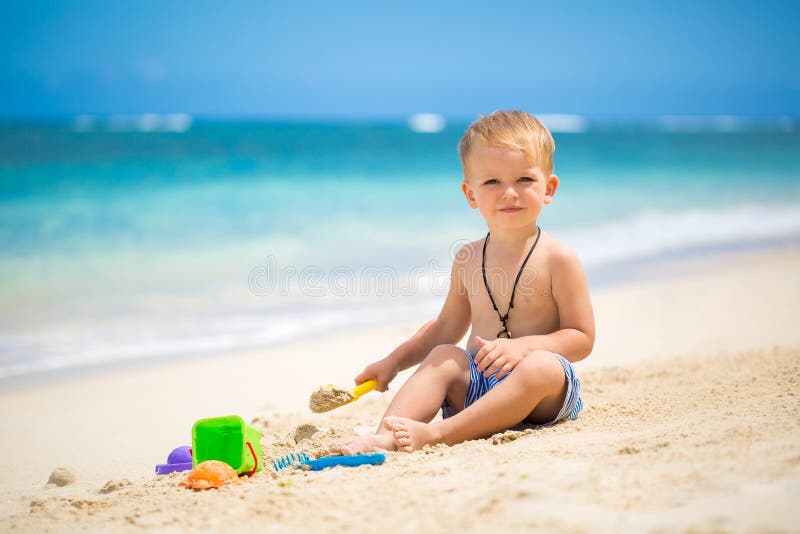 Cute baby boy playing with beach toys on tropical beach