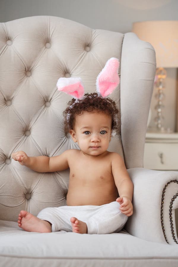 Cute baby with bunny ears on the chair in the room