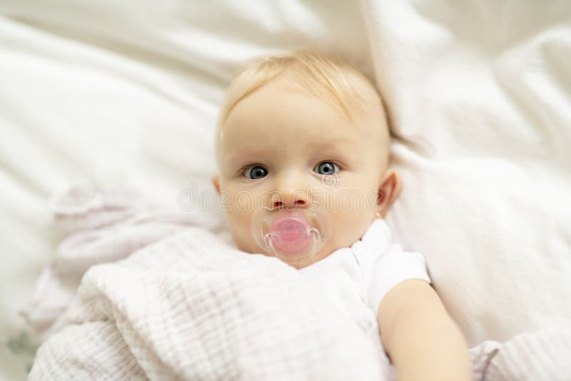 A Cute Baby with Pacifier Lying on a White Bed Stock Photo Image of