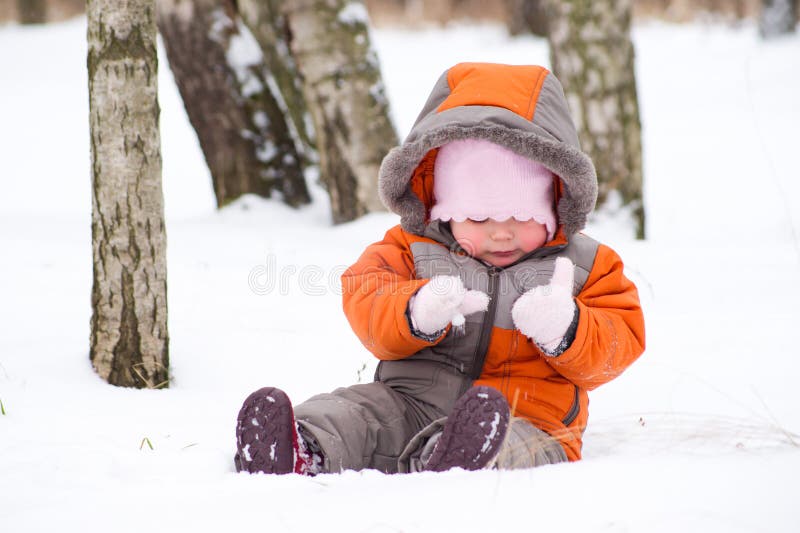 Cute baby sit on snow and play with mittens