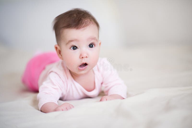 Cute baby under 1 year old with surprised expression wearing pajamas crawling in bed at home close up. Childhood.