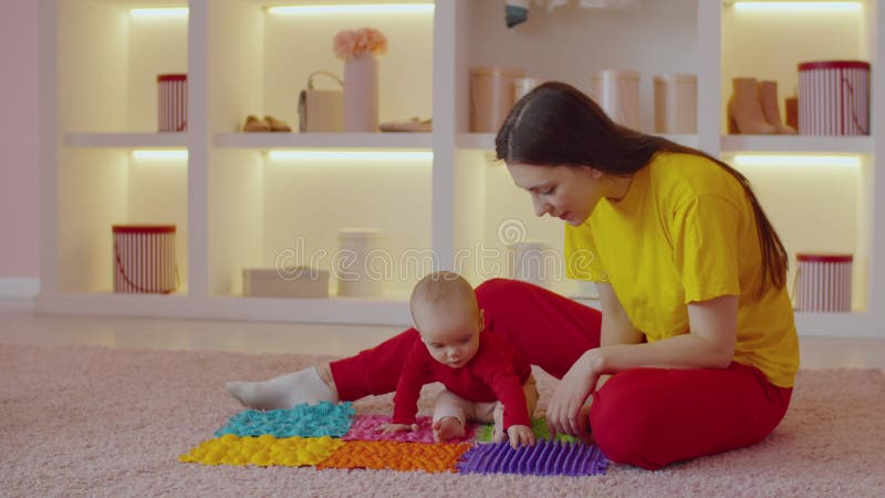 Cute barefoot infant baby with help of mother walking on orthopedic massage mat