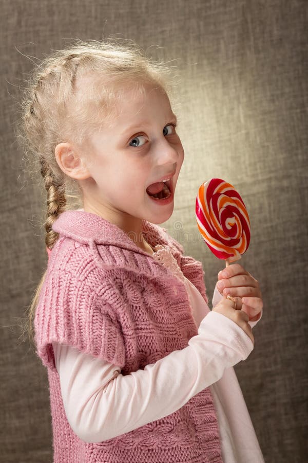 Cute beautiful blonde little girl holding lollipop. Bright portrait