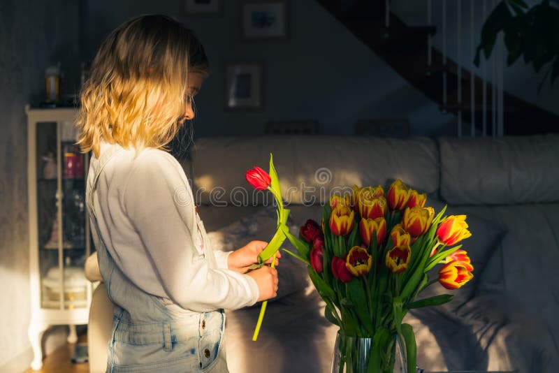 Cute beautiful little toddler girl making flower bouquet. Little girl putting tulip to the bouquet in a vase. Making gift bunch