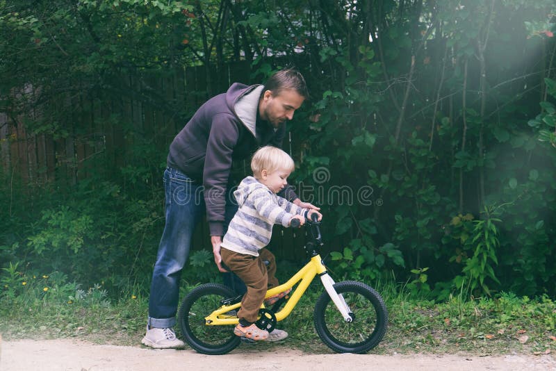Cute blond boy learning to ride bicycle. Father teaching his little child to ride bike in spring summer park. Happy family moments