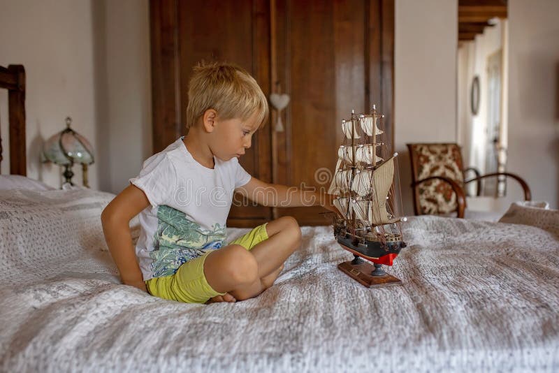 Cute blond child, boy, playing at home with toys, ship, dolls