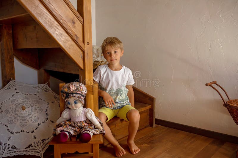 Cute blond child, boy, playing at home with toys, ship, dolls