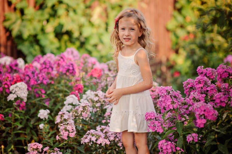 Cute blonde child girl playing in summer blooming garden