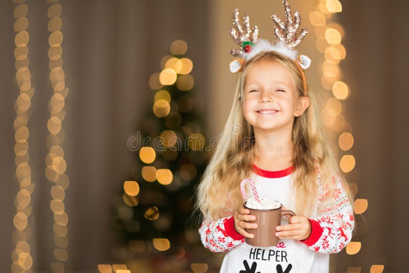 Cute blonde girl 5 years old drinking hot cacao near Christmas tree. Bedroom decorated with Christmas garlands. home