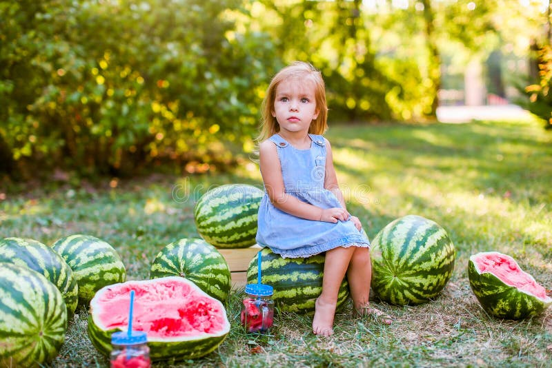 Cute blonde little girl sitting with watermelons around in a park. Summer, fruits, harvest concept