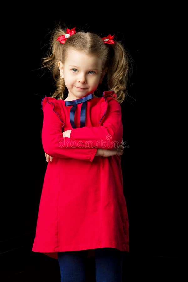 Cute blonde little girl standing on black backdrop