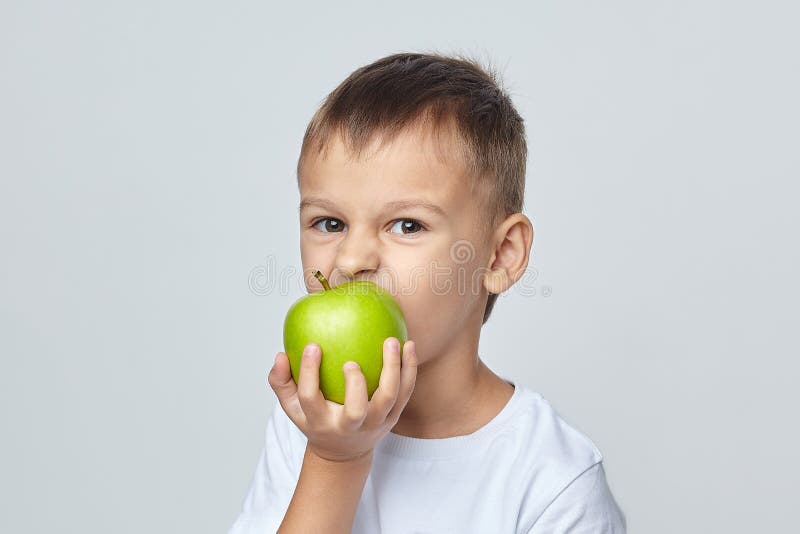 Cute boy bites a green Apple. photo session in the Studio on a white background