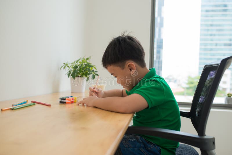 Cute boy doing homework, coloring pages, writing and painting. Children paint. Kids draw. Preschooler with books at home. stock photos Cute boy doing homework, coloring pages, writing and painting. Children paint. Kids draw. Preschooler with books at home. stock photos