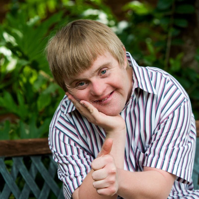 Cute boy with down syndrome doing thumbs up in garden. stock photo Cute boy with down syndrome doing thumbs up in garden. stock photo