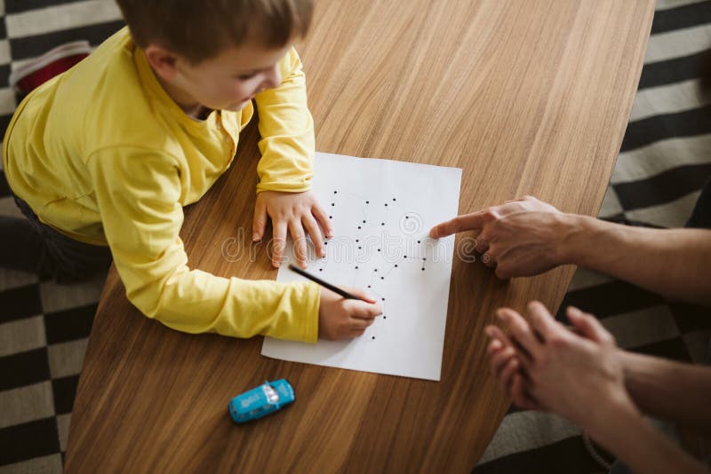 Cute boy kneeling on the floor and connecting dots on a piece of paper