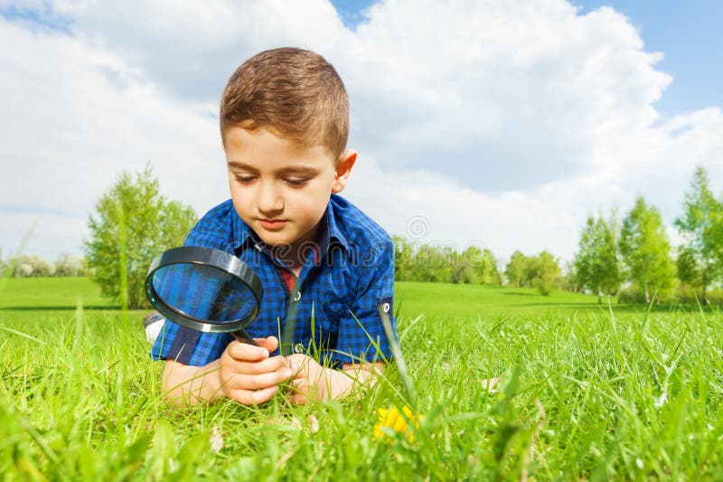 Cute boy with magnifier lays on the green grass