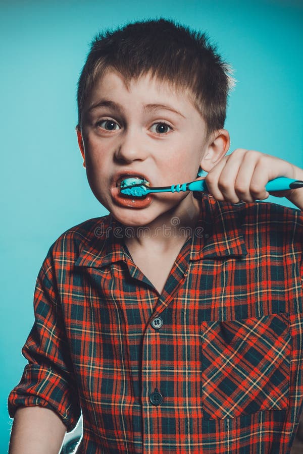 A cute boy in a pajamas brushes teeth with toothpaste before bedtime on a blue background stock image A cute boy in a pajamas brushes teeth with toothpaste before bedtime on a blue background stock image