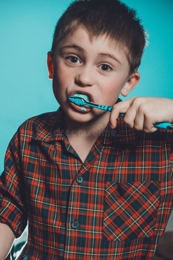 A cute boy in a pajamas brushes teeth with toothpaste before bedtime on a blue background stock photo A cute boy in a pajamas brushes teeth with toothpaste before bedtime on a blue background stock photo