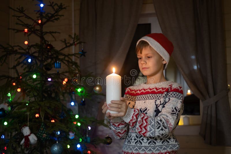 Cute boy in a red cap standing at the window and Christmas tree with a candle in his hands royalty free stock photography Cute boy in a red cap standing at the window and Christmas tree with a candle in his hands royalty free stock photography