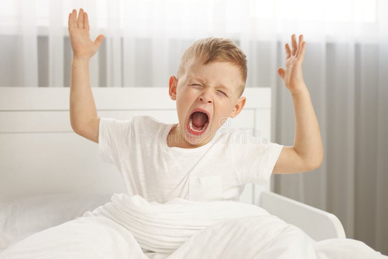 The Cute Boy Wakes Up with His Arms Outstretched and Yawns. Stock Photo
