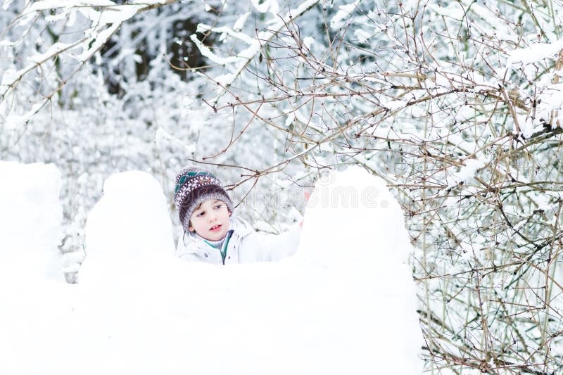 Cute boy in white jacket playing in a snow fort