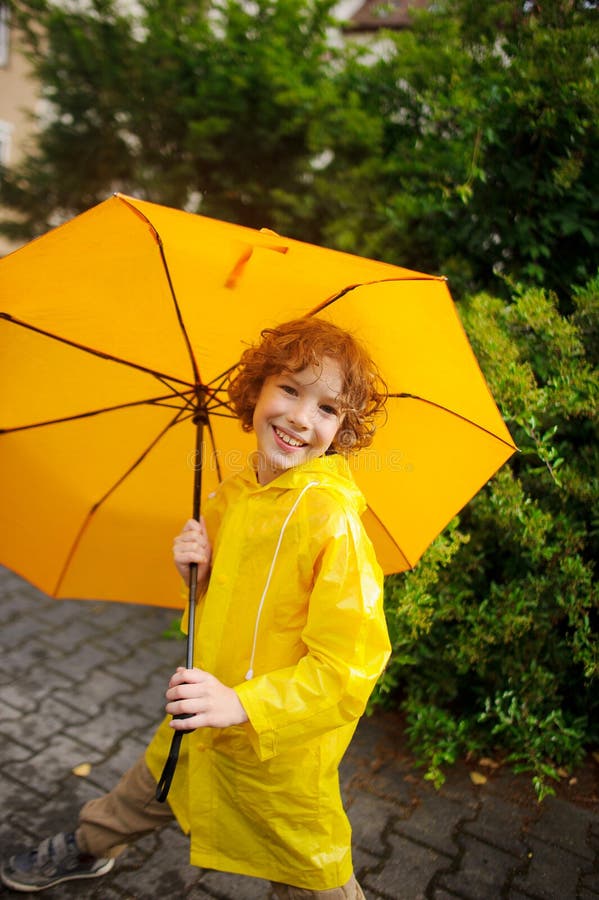 The cute boy of 8-9 years under a yellow umbrella.