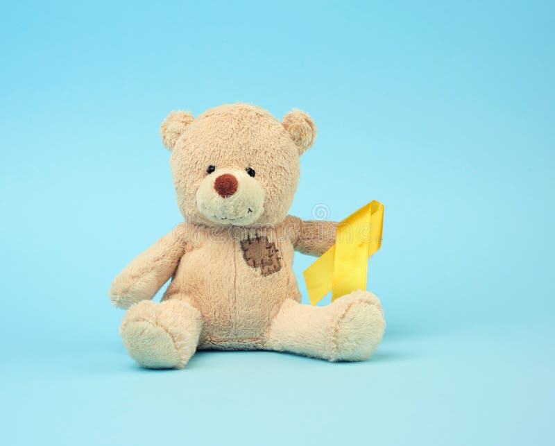 Cute brown teddy bear with a patch holds a silk yellow ribbon in the shape of a loop