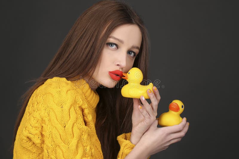 Cute brunette woman with red lips kissing yellow rubber ducks