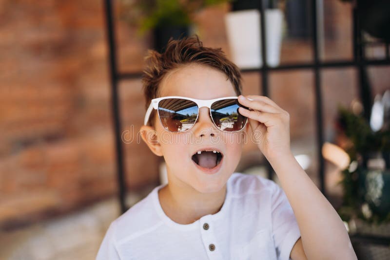 Cute cauasian boy in white tee shirt and sunglasses posing for camera and showing his lost tooth.