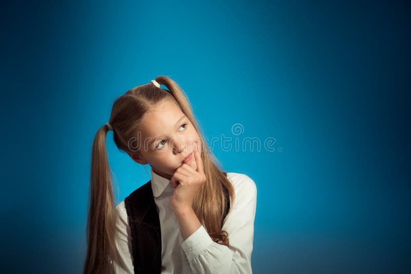 Cute Caucasian schoolgirl thought about the task, putting hand to her face, looking to the side stock photo Cute Caucasian schoolgirl thought about the task, putting hand to her face, looking to the side stock photo