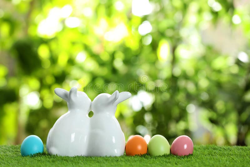 Cute ceramic Easter bunnies and dyed eggs on grass against blurred background, space for text stock photo Cute ceramic Easter bunnies and dyed eggs on grass against blurred background, space for text stock photo