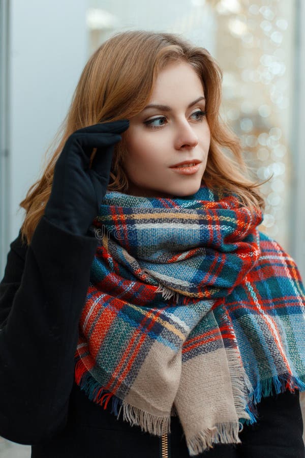 Cute charming young woman with blond hair in a stylish winter coat with a woolen vintage scarf in black gloves posing on the