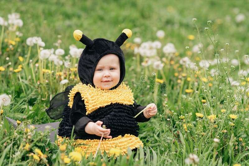cute and cheerful portrait of little child sitting in blooming flowers of dandelion in yellow bee costume.