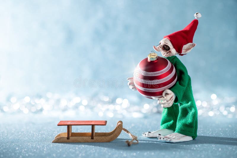 Cute Cheerful Santas Helper Elf Loading Christmas Bauble Onto Santas Sleigh. North Pole Christmas Scene. Elf at work. stock photos Cute Cheerful Santas Helper Elf Loading Christmas Bauble Onto Santas Sleigh. North Pole Christmas Scene. Elf at work. stock photos