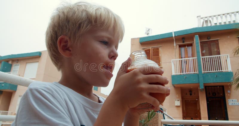 Cute child boy drinking organic tomato juice from glass outdoors