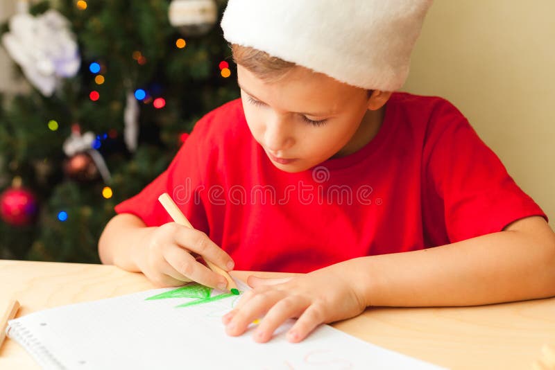 Cute child boy write letter to Santa, Christmas tree on background