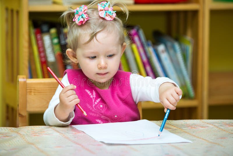 Cute child girl drawing with colorful pencils in preschool at table in kindergarten