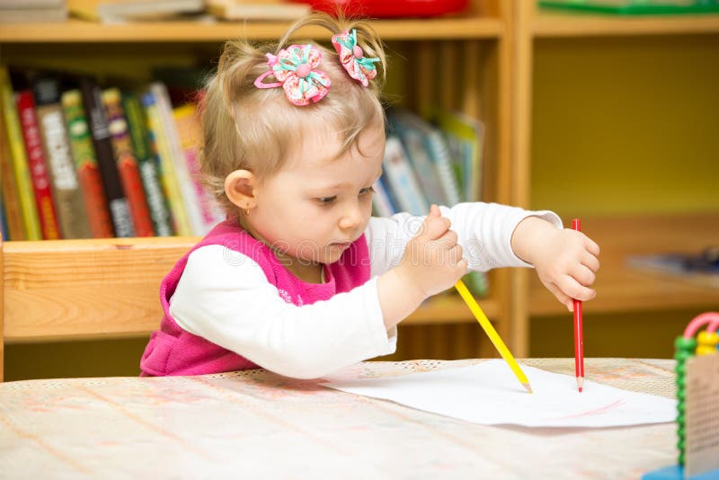 Cute child girl drawing with colorful pencils in preschool at table in kindergarten