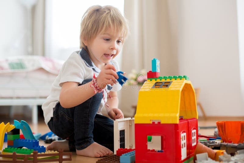 Cute child, playing with colorful toy blocks. Little boy building house of block toys sitting on the floor in sunny spacious