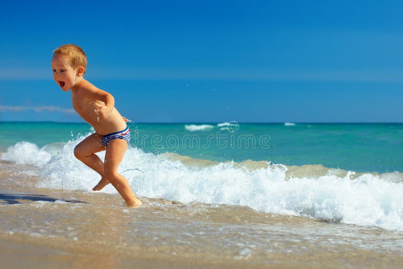 Cute child running from sea waves on beach