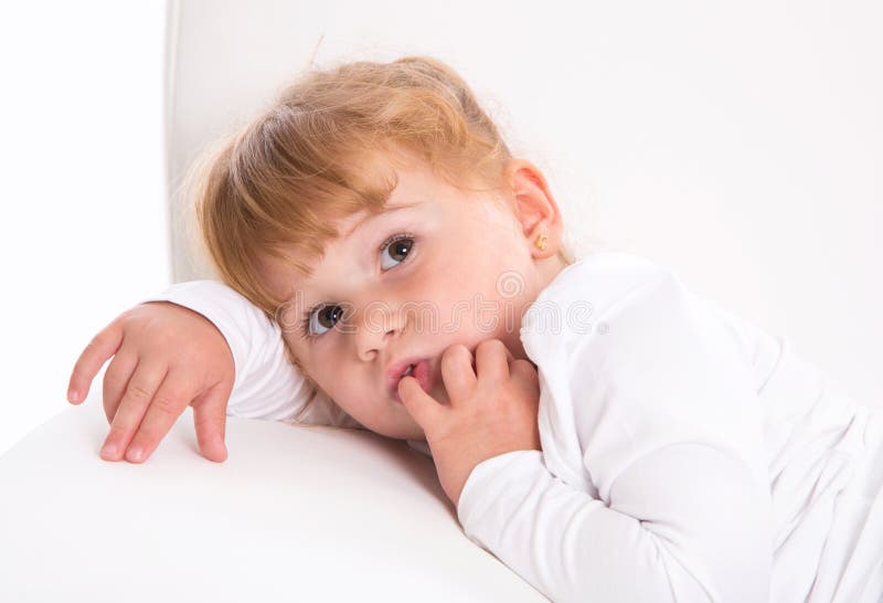 Cute child - shy girl lying on white sofa sucking thumb or finger stock photos Cute child - shy girl lying on white sofa sucking thumb or finger stock photos
