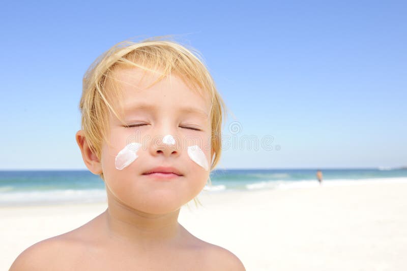 Carino bambino prendere il sole con la protezione solare in faccia alla spiaggia, sorridente.