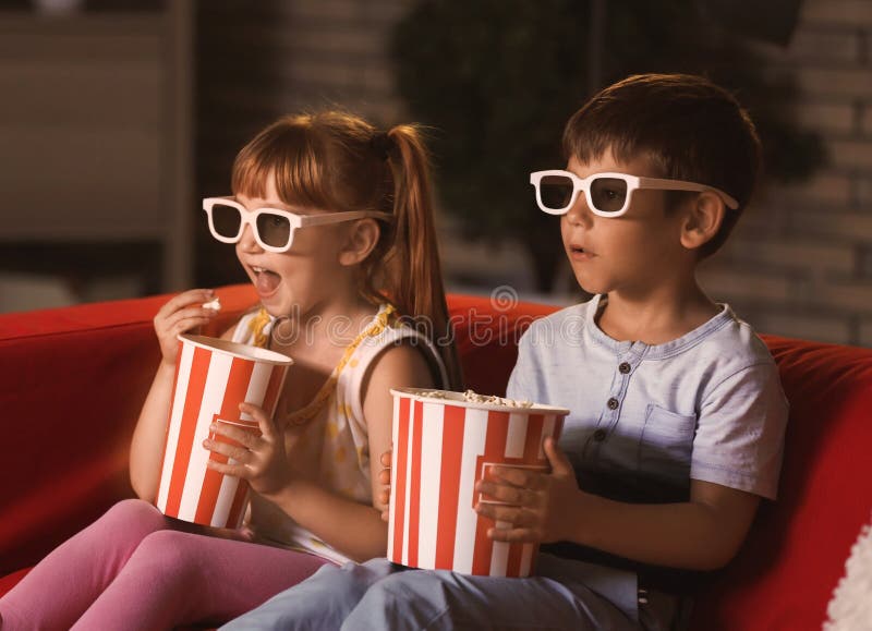 Cute children in 3d glasses watching movie on sofa in evening