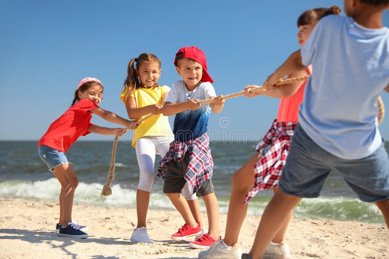 Cute children pulling rope during tug of war game on beach. Summer camp