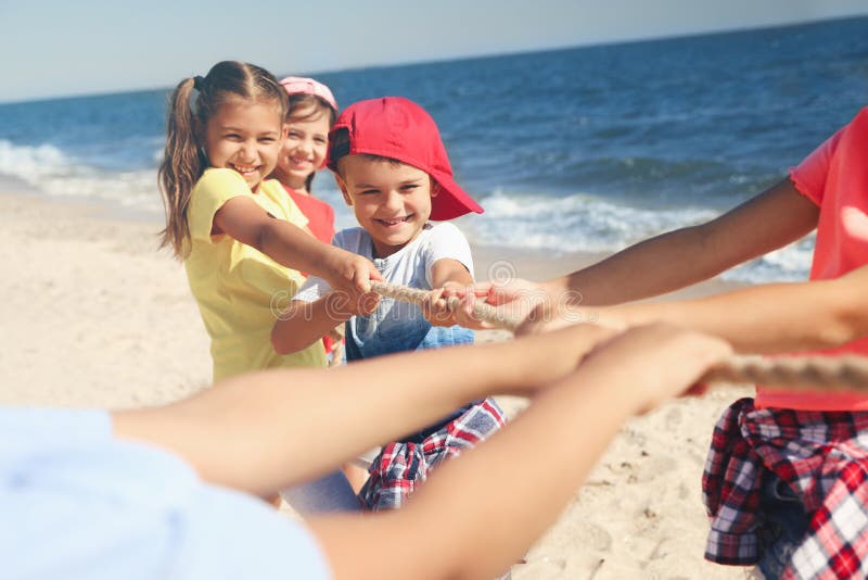 Cute children pulling rope during tug of war game on beach. Summer camp