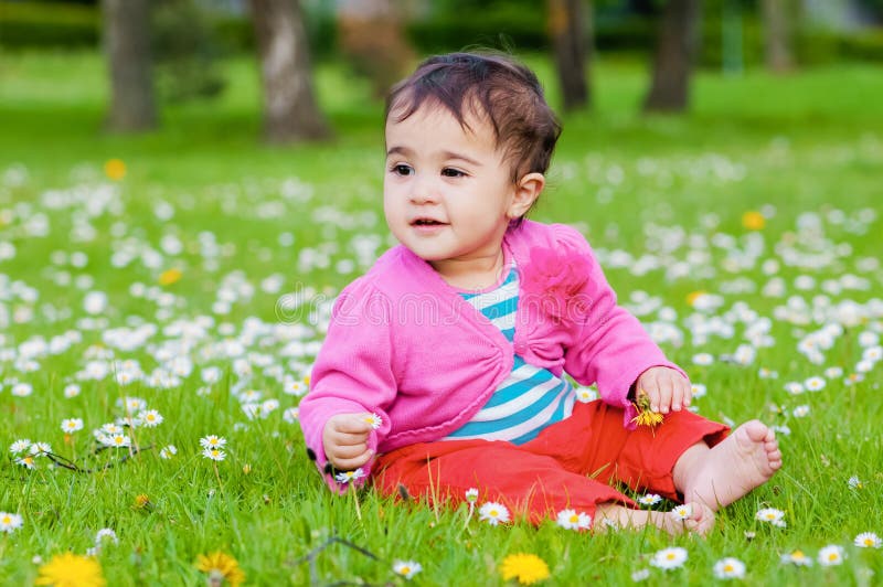 Cute chubby toddler sitting on the grass smiling exploring nature outdoors in the park stock photography