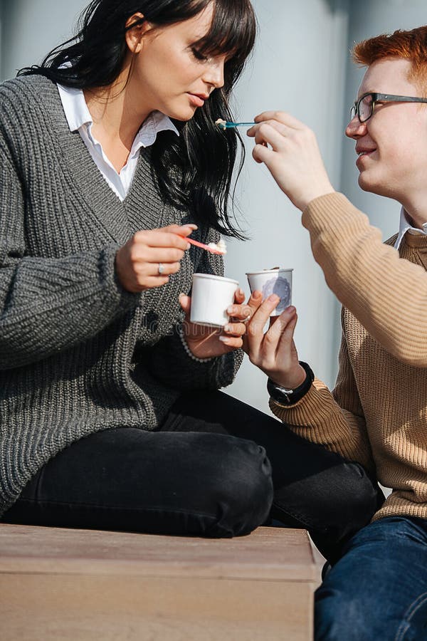 Cute couple sitting outdoors, feeding each other ice cream with spoon